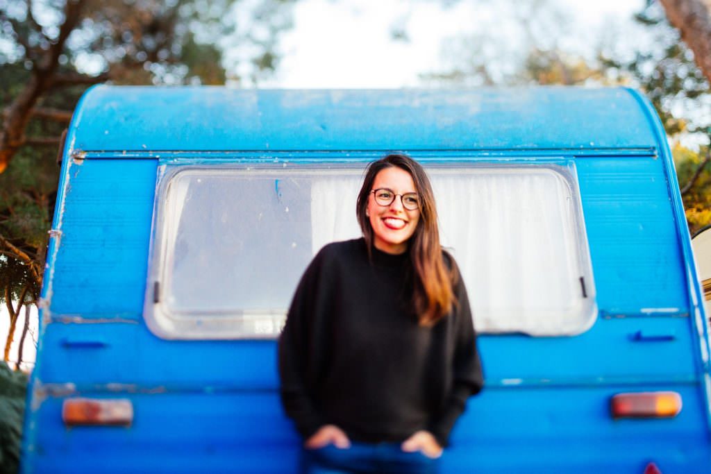 Elsa, photographe, souriante devant une caravane bleue